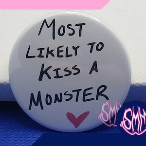 Puede incluir: Botón blanco con texto negro que dice "Most Likely to Kiss a Monster" con un corazón rosa en el centro.