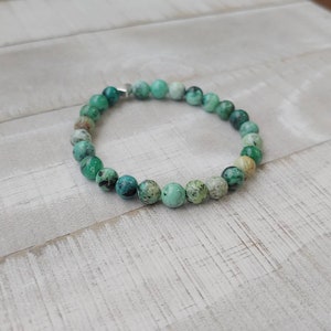 Puede incluir: Una pulsera de cuentas con cuentas redondas de color turquesa con motas verdes oscuras y blancas. La pulsera est&aacute; ensartada en una banda flexible y tiene un cierre plateado. Las cuentas tienen aproximadamente 0,8 cm de di&aacute;metro.