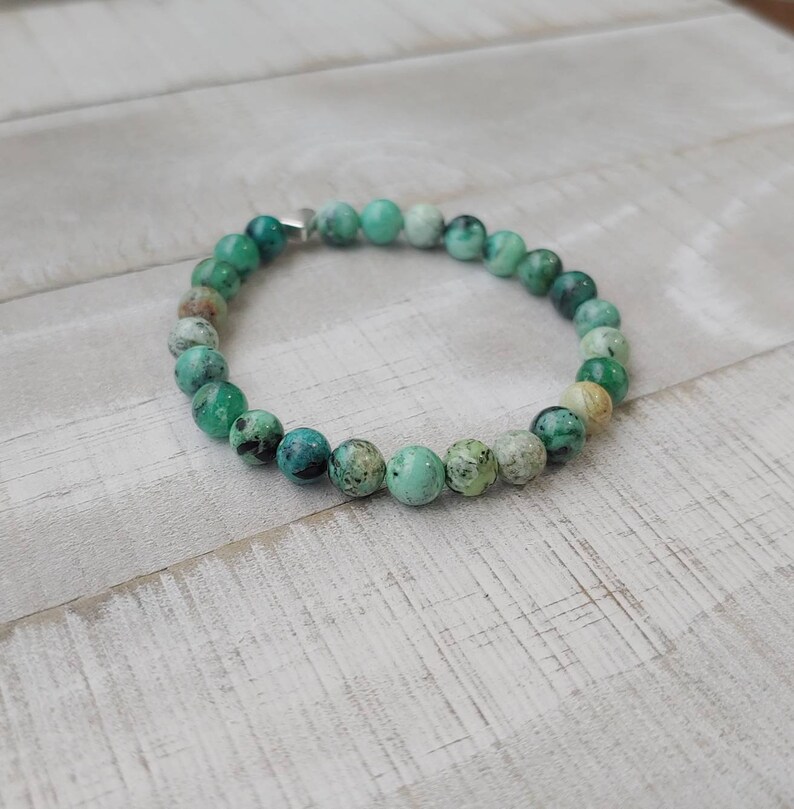 Puede incluir: Una pulsera de cuentas con cuentas redondas de color turquesa con motas verdes oscuras y blancas. La pulsera est&aacute; ensartada en una banda flexible y tiene un cierre plateado. Las cuentas tienen aproximadamente 0,8 cm de di&aacute;metro.