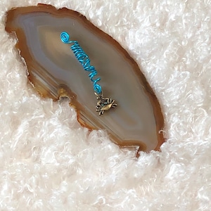 Puede incluir: Un espiral de pelo de alambre azul con un dije de cangrejo dorado sobre una rebanada de ágata marrón claro.