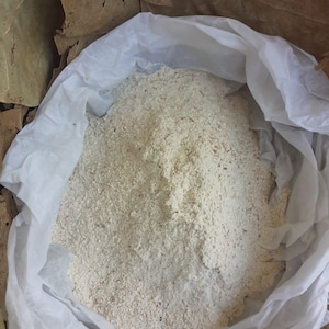 Peut inclure: Un sac en papier blanc rempli d'une grande quantité de poudre brun clair. La poudre est probablement une sorte de farine ou de céréale.