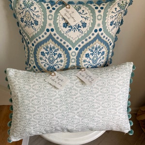 Puede incluir: Dos almohadas decorativas con patrones azules y blancos. La almohada más grande tiene un patrón floral azul y blanco con una etiqueta que dice "It something special". La almohada más pequeña tiene un fondo blanco con un patrón floral azul claro y una etiqueta que dice "Bispoke Cotton Cover".