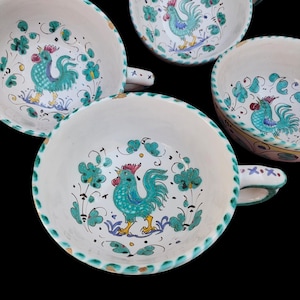 May include: Set of four white ceramic mugs with green and blue rooster designs. Each mug has a handle and a green and white rim.