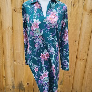 Puede incluir: Un vestido largo de color turquesa con mangas largas y estampado floral con flores rosas y moradas. El vestido tiene cuello y mangas largas.