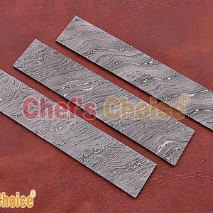 May include: Three rectangular pieces of patterned metal, with a swirling, marbled design in shades of gray. The metal pieces are arranged in a staggered pattern on a brown leather surface.