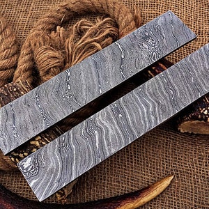 May include: Two long, rectangular pieces of metal with a wavy, patterned surface. The metal is a dark gray color with a silver sheen. The pieces are lying on a brown burlap surface.