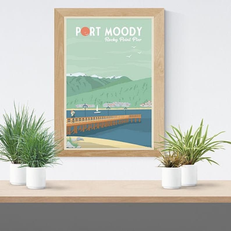May include: A framed art print featuring a coastal scene with a pier extending into the water. The print has the text "PORT MOODY Rocky Point Pier" at the top. The artwork is in a light wood frame and is displayed on a wooden shelf with potted plants.