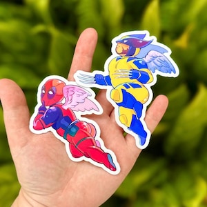 May include: Two colourful cartoon superhero stickers. One sticker features a red and blue Deadpool with pink angel wings. The other sticker features a yellow and blue Wolverine with blue angel wings.