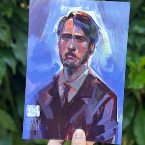 May include: A portrait print of a man in a dark suit and tie, set against a blue backdrop. The artwork displays a painterly style with visible brushstrokes and the text "JENNIE PLANET". The print is held by a hand.