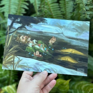 Op de afbeelding: Een kunstafdruk met een man in een groene jas die in het water drijft. Het kunstwerk heeft een schilderkunstige stijl met een gedempte kleurenpalet van groen, blauw en geel. De afdruk wordt door een hand vastgehouden tegen een achtergrond van groen gebladerte.