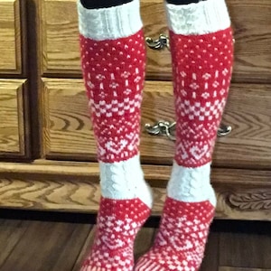 May include: Red and white knee-high socks with a patterned design. The socks feature a white cuff and foot, with a red body adorned with white geometric shapes. The socks are worn over black leggings.