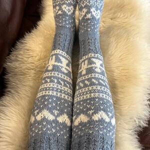 May include: Light blue knitted socks with a white snowflake design. The knee-high socks are displayed on a white fur rug. The socks are made from a soft, warm material, perfect for cold weather.