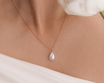 May include: A woman with red hair wearing a white off-the-shoulder top and a gold necklace with a pearl pendant. She is holding a white tulip.
