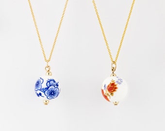 Könnte beinhalten: Vier goldene Halsketten mit unterschiedlich großen Porzellan-Anhängerperlen. Die Perlen sind mit blauen und weißen Blumenmustern oder roten und weißen Blumenmustern verziert. Die Perlen messen 8 mm, 12 mm, 12 mm und 10 mm.