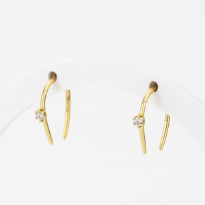 May include: A pair of gold hoop earrings with a small clear stone accent.