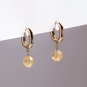 Könnte beinhalten: Goldene Creolen mit einem baumelnden gelben Edelstein.