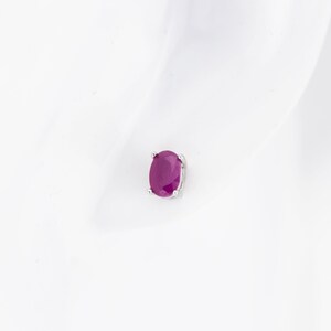 May include: A single ruby stud earring in a silver setting. The ruby is oval shaped and a deep red color.