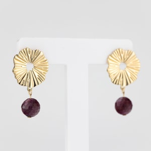 May include: A pair of gold earrings with a textured, circular design and a dangling purple gemstone.