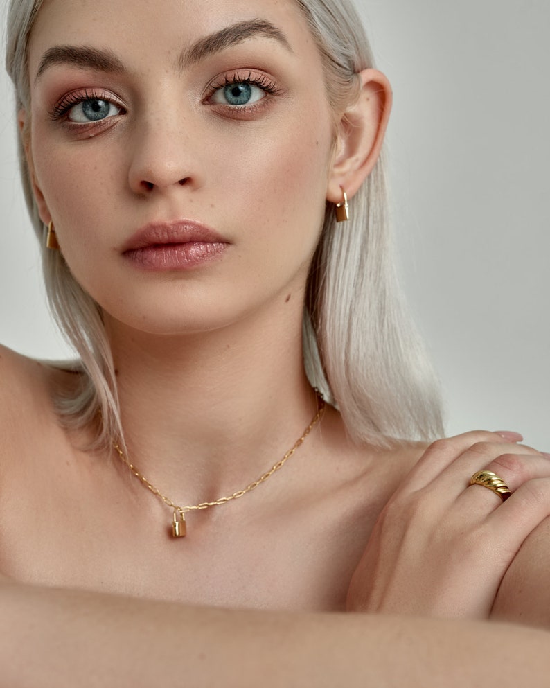 Model is wearing Gold Lock Hoops as an earring and as a padlock charm on a necklace
