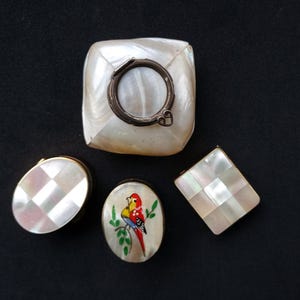 Puede incluir: Cinco pequeñas cajas decorativas hechas de nácar. Las cajas son de varias formas y tamaños, y algunas tienen diseños pintados. Una caja tiene un pequeño lazo metálico redondo en la parte superior.
