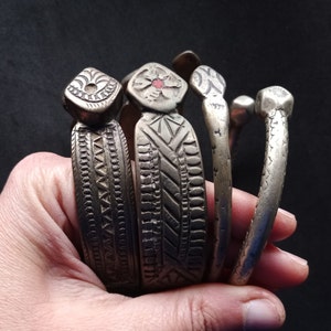May include: Four silver bracelets with intricate engraved designs. The bracelets are stacked on top of each other and have a slightly worn look.