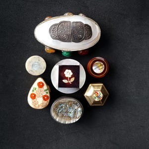 Puede incluir: Una colección de siete pequeñas cajas decorativas con diversos diseños y materiales. Las cajas están hechas de madera, metal y concha. Algunas de las cajas tienen diseños florales, mientras que otras tienen patrones geométricos. Las cajas son todas de diferentes tamaños y formas.