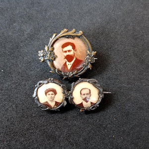 Puede incluir: Tres broches antiguos de tono plateado con retratos de vidrio ovalados. La broche superior presenta a un hombre con barba y bigote, mientras que las dos broches inferiores presentan a una pareja.