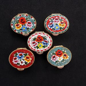 May include: Five oval-shaped metal trinket boxes featuring intricate micro-mosaic floral designs on their lids. Each box displays a unique colour scheme of red, teal, or white backgrounds with colourful flower patterns in red, yellow, blue, and white.