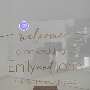 Może przedstawiać: Przezroczysty znak akrylowy z pozłacanymi literami, na którym widnieje napis "welcome to the wedding of Emily and John Saturday March 19th 2022".