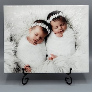 May include: A white ceramic tile with a photo of two sleeping babies wrapped in white blankets. The babies are wearing white headbands with bows. The tile has the text "BRYNNLEY" and "KYN SLEY" printed on it. The tile also has the year "2021" printed on it.