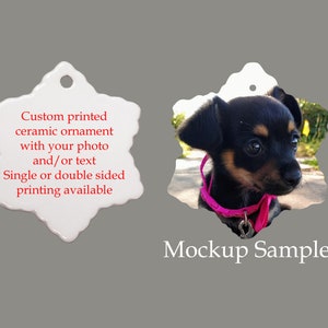 May include: White ceramic snowflake ornament with a custom printed image of a small black and brown dog wearing a pink collar. The ornament is blank on the other side and has a hole for hanging. The text "Custom printed ceramic ornament with your photo and/or text Single or double sided printing available" is printed on the blank side. The text "Mockup Sample" is printed below the ornament.