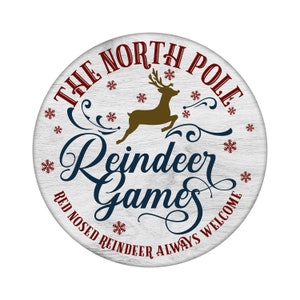 May include: A white wooden round sign with the text "THE NORTH POLE Reindeer Games RED NOSED REINDEER ALWAYS WELCOME" in red and blue lettering. A brown reindeer silhouette is in the center of the sign.