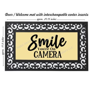 May include: Black doormat with a white and black decorative border. The center of the mat is a light yellow color with the text "Smile You're On CAMERA" in black.