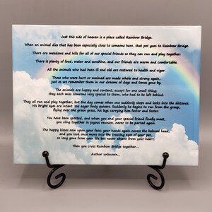 May include: A white ceramic tile with a blue sky and white clouds background. The tile features a poem about the Rainbow Bridge, a place where pets go after they die. The poem is written in black text and includes a rainbow.