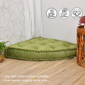 May include: A sage green corner floor cushion featuring a tufted design with multiple fabric buttons across the top surface. The cushion has a thick, structured border and a soft, velvet-like texture, designed to fit into a corner space.