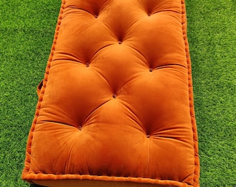 May include: A rectangular floor cushion in a vibrant orange velvet fabric. The cushion features a tufted design with twelve evenly spaced buttons creating a dimpled surface texture. The edges are finished with a piped border detail.