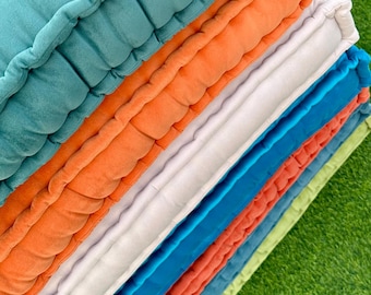 May include: A stack of square floor cushions featuring tufted detailing and piped edges. The cushions are arranged in a vertical column, showcasing a vibrant color palette including teal, orange, white, blue, and light green fabric textures.
