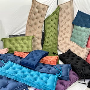 May include: Assortment of tufted cushions in various colours, including green, blue, pink, and beige. The cushions are made of fabric and have a button tufted design.