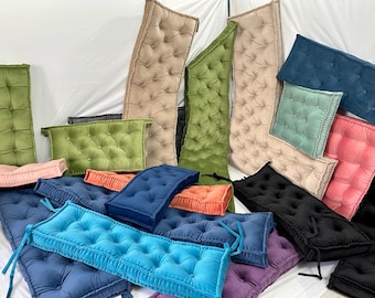 May include: A collection of rectangular tufted cushions in various colors including olive green, beige, navy blue, bright blue, black, pink, and purple. Each cushion features a button-tufted surface, soft fabric texture, and attached fabric ties.