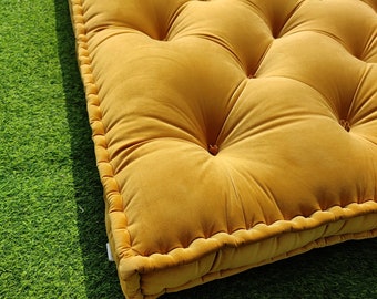 May include: A rectangular mustard yellow floor cushion featuring a tufted surface with multiple fabric-covered buttons arranged in a grid pattern. The cushion has thick, piped edges and a soft, velvet-like texture across the entire top surface.