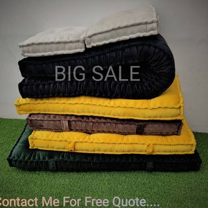 May include: A stack of six cushions in various colors, including black, brown, yellow, and green. The cushions are made of a soft, quilted fabric and have a tufted design. The top cushion is rolled up and has the words "BIG SALE" printed on it.