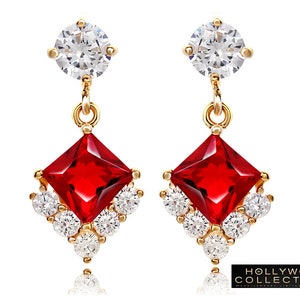 May include: Gold earrings with a red square gemstone and a smaller round clear gemstone at the top. The earrings have a delicate design with smaller clear gemstones surrounding the red gemstone.