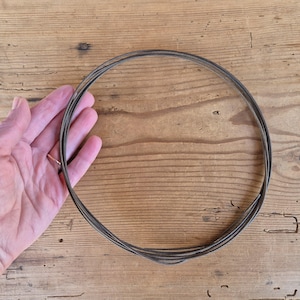Op de afbeelding: Een doorlopende spoel van dun, donkerbruin leren koord in een cirkelvorm. Het koord heeft een gladde, matte textuur en is flexibel, waardoor het meerdere overlappende lussen vormt die een uniform, rond silhouet creëren voor diverse toepassingen.
