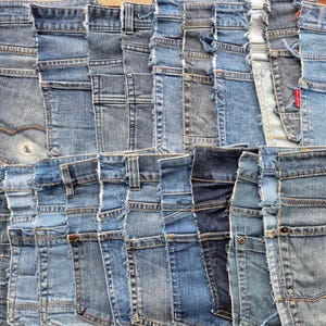 Può includere: Una collezione di vari campioni di tessuto denim disposti a griglia. I pezzi presentano diverse tonalità di blu, dal lavaggio chiaro all'indaco scuro, con cuciture visibili, bordi sfilacciati, rivetti metallici e passanti per cintura.