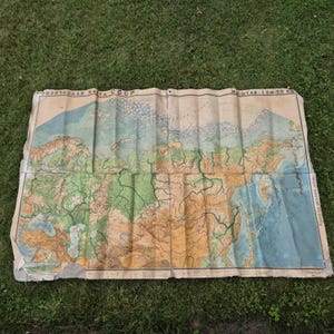 May include: A large, folded physical map of the USSR featuring topographical details in shades of green, brown, and blue. The map includes the Cyrillic text "ФИЗИЧЕСКАЯ КАРТА СССР" and "МАСШТАБ: 1 СМ-50 КМ" printed along the top edge on a light beige paper background.