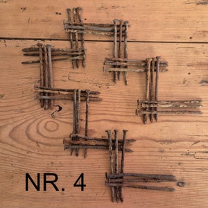 Può includere: Primo piano di una superficie in legno con un motivo di chiodi arrugginiti disposti in un design geometrico. I chiodi sono disposti a forma di croce con il testo "NR. 4" sotto il disegno.