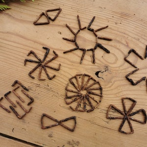May include: A collection of eight rusty metal starburst shapes arranged on a wooden surface. The shapes are made of nails and are different sizes and designs.
