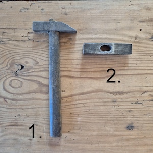 May include: Two vintage carpentry tools: a hammer and a mallet. The hammer has a gray metal head and a wooden handle. The mallet is rectangular with a hole in the center. Both tools are on a wooden surface.
