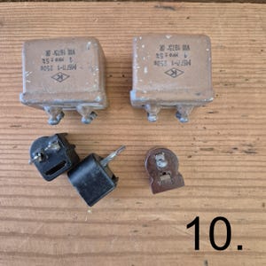 K&ouml;nnte beinhalten: Zwei rechteckige braune elektronische Kondensatoren mit Metallanschl&uuml;ssen und aufgedrucktem Text, darunter MБГП-1 250B 1 MKF &plusmn;5% VIII 1973R, sowie drei kleinere schwarze und braune elektrische Bauteile mit Metallstiften auf einer Holzoberfl&auml;che.