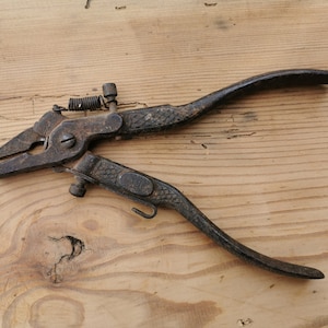 Op de afbeelding: Een vintage zaagzetter van donkerbruin metaal met een getextureerde handgreep, een kleine spanveer en een verstelbaar schroefmechanisme. Het gereedschap heeft een verweerde, geoxideerde afwerking met zichtbare sporen van ouderdom en gebruik.